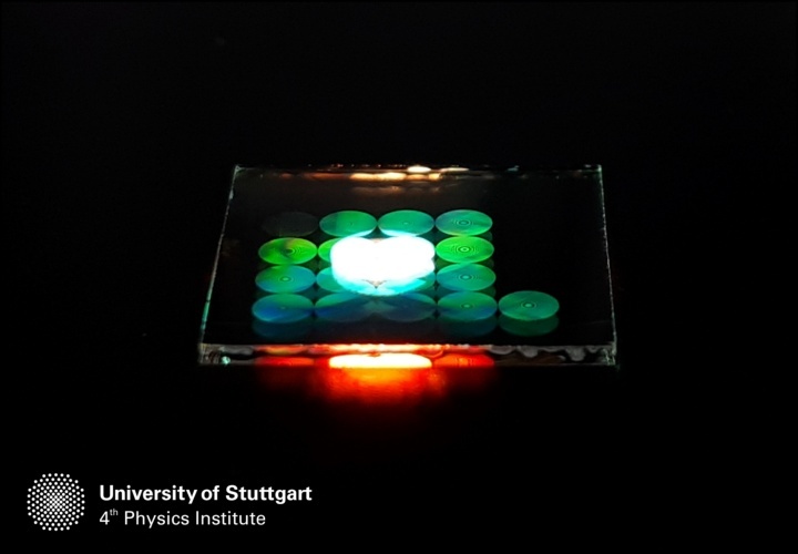 Photograph of several metalenses on a glass substrate, illuminated from the top with white light.